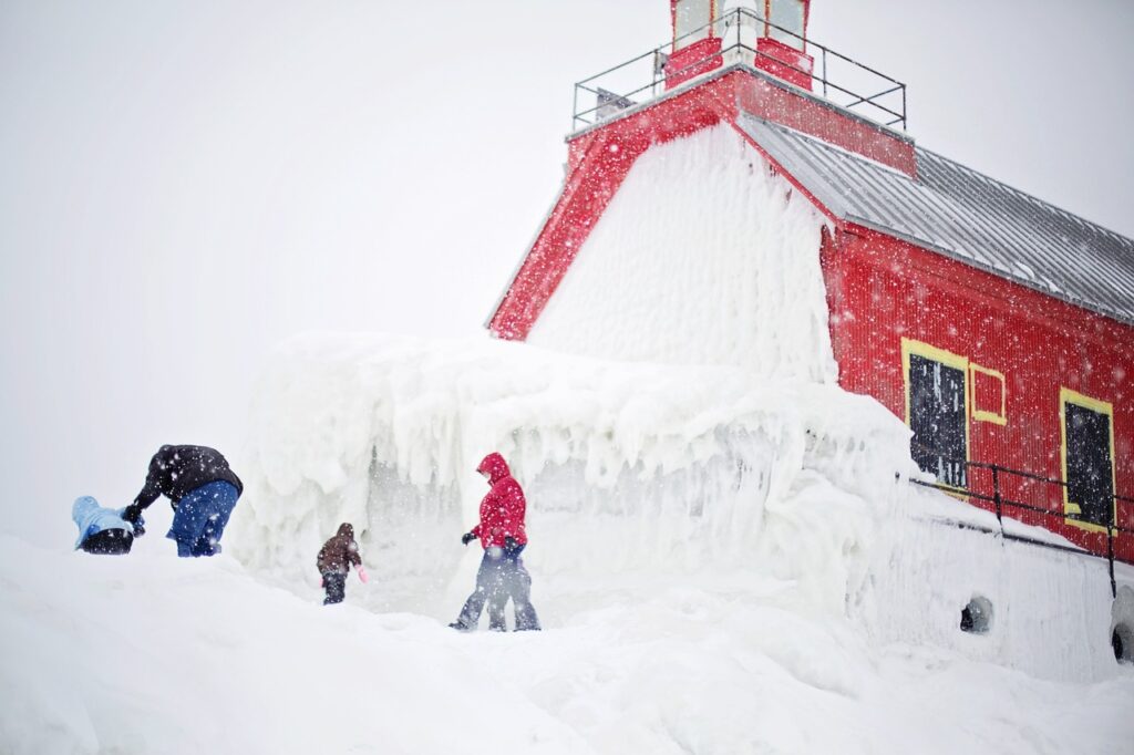 Family playing in front of lighthouse in winter in Michigan